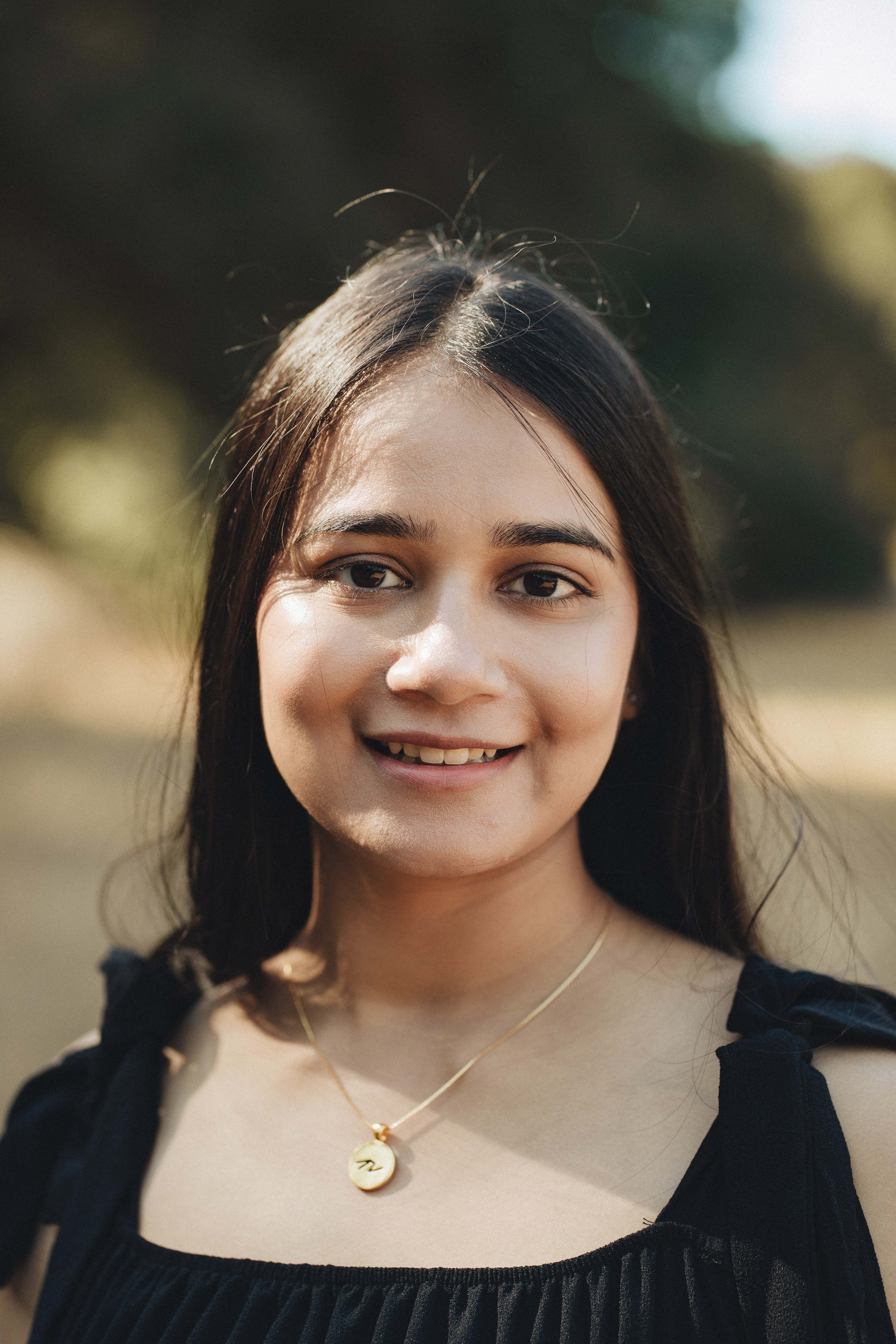 Professional portrait of Nitika, a visual designer with dark hair wearing a black top and gold necklace, smiling warmly
